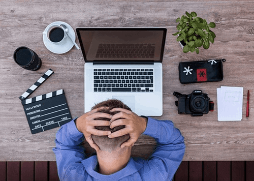 A man holding his head whilst using his laptop.