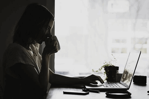 Girl drinking whilst working on her laptop.