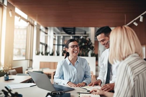 three employees stood laughing around a laptop