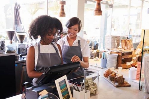 Two cafe workers using a till while smiling